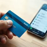 Mão a segurar um cartão bancário ao lado de um telemóvel, durante a ativação do cartão